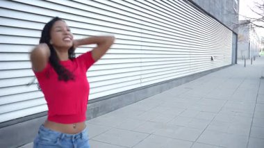 Neşeli genç bir kadın açık hava ortamında mutlulukla kıvrılır, kaygısız ruhunu gururla sergilerken canlı kırmızı bir bluz ve şık kot pantolon giyer.