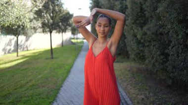 Neşeli ve neşeli bir kadın şık, canlı kırmızı bir tulum giyiyor ve büyüleyici bir açık hava ortamında enfes bir enerji ile zarif bir şekilde dans ediyor. Yeşillik ve doğal güzelliklerle çevrili.