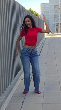 Şık, genç bir kadın açık havada canlı kırmızı bir bluzla poz veriyor ve kotları da ışıl ışıl. Günlük kıyafetleri karizmatik kişiliğini ve gençlik ruhunu gözler önüne seriyor. Eğlenceli bir gün için mükemmel.