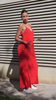 Şık bir kadın dikkat çekici ve canlı kırmızı bir tulum içinde modern dokulu bir duvara karşı zarif bir şekilde dizilmiş, zarif ve çağdaş moda duyarlılığını sergiliyor.