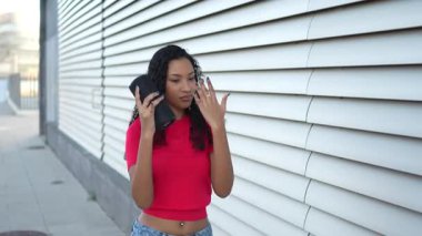 Parlak kırmızı bluzlu genç bir kadın açık havada müzik dinlemekten hoşlanıyor, bir hoparlör tutuyor ve gülümsüyor, eğlencenin özünü yakalıyor. Bu sahne yaşam tarzı ve müzik içeriği için mükemmel.