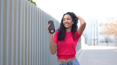 Canlı ve enerjik genç bir kadın dışarıda neşeli bir şekilde dans ediyor, kulaklık takıyor, enerjik ve dinamik bir şehir ortamında kaygısız ve neşeli bir tavır sergiliyor.