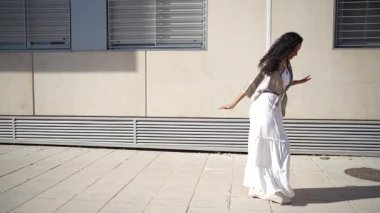 Güzel beyaz bir elbise giymiş neşeli bir dansçı zarif ve zarif bir şekilde dışarıda gösteri yapar. Basit ve minimalist bir arka plana karşı sanatsal yeteneğini ve özgürlüğünü sergiler.