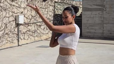 Neşeli genç bir kadın, neşe ve neşe saçan, neşe saçan ve zarafet saçan neşeli ve şık yaz kıyafetlerini gösterirken mutlu bir şekilde elini sallıyor.