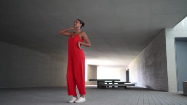 Canlı bir şehir sahnesinde, kırmızı tulumlu şık bir dansçı zarif hareketleriyle izleyicileri büyülüyor, topluluğun ritmini yükseltiyor ve çevresine bulaşıcı enerji getiriyor.