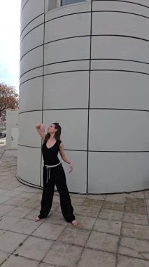 Yetenekli bir dansçı, seyirciyi hareketli ve etkileyici siyah kıyafetleriyle cezbeder ve modern şehir arkaplanına karşı çarpıcı bir kontrast yaratır.