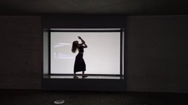 Bir dansçının zarif silueti, çağdaş bir galeri ortamında, temiz, minimalist bir arkaplana karşı hareket ve zarafeti vurgulayan etkileyici bir performans sergiliyor.