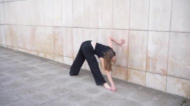 Yetenekli bir dansçı, etkileyici esneklik ve yaratıcılığını koreografi ve performanslarında göstererek, dokulu bir duvara karşı anlamlı hareketler ve zarif pozlar sergiler.