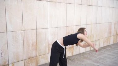 Becerikli bir dansçı, dokulu bir duvara karşı akışkan hareketler sergiler, kentsel bir ortamda çağdaş dansların ifade edilebilirliğini vurgular, büyüleyici bir yaratıcılık ve hareket atmosferi yaratır.