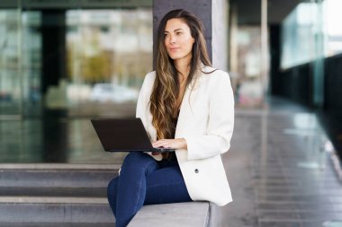 Kendine güvenen profesyonel bir kadın dizüstü bilgisayarla şık bir şekilde oturmuş, canlı ve modern bir çalışma alanı atmosferi sergiliyor, iş dünyası, yenilik ve işbirliği fikirleri ile ilgili konular için mükemmel.