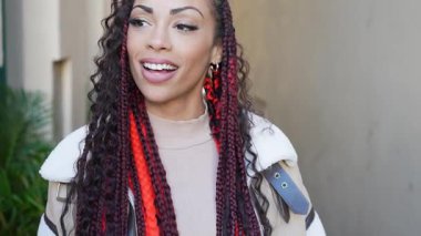 Şık ve şık bir genç kadın, saç stili ve şık elbisesini gururla sergilerken renkli ve enerji dolu canlı bir şehir zeminine poz veriyor.