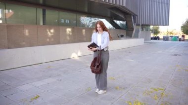 Odaklanmış bir öğrenci dışarıda sakin bir ortamda elinde bir kitapla dikiliyor ve dikkatlice yukarı bakıyor. Hepsi de güzel modern mimari ve canlı sonbahar yapraklarıyla çevrili.