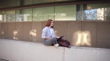 Enerjiyle dolu canlı bir şehirde, genç bir kadın şık bir bankta mutluluğu bulur, tabletine dalmış, teknolojiyle çevresini çevreleyen hareketli şehir ortamını birleştirir