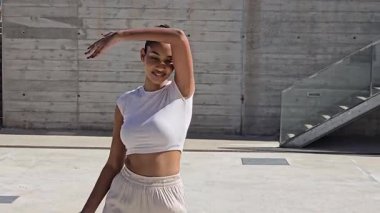 Havalı bir kadın ellerini modern beton zemine kaldırarak dışarıda poz veriyor, canlı bir şehir ortamında şık bir kıyafet sergiliyor, güzelliğini ve yaşam tarzını ön plana çıkarıyor.