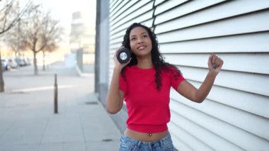 Neşeli genç bir kadın dışarıda portatif bir hoparlörle neşeyle dans ediyor, müziğe olan aşkını, deneyimini geliştiren çarpıcı modern bir mimari zemine karşı kucaklıyor.