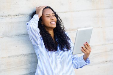 Tabletini kontrol ederken hayal kırıklığını ifade eden bir kadın, beton duvara yaslanmış, modern hayatın pek çok insanın özdeşleştirebileceği bir anını sergiliyor.