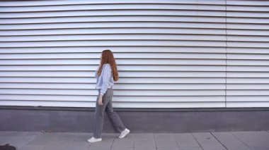 Şık ve kendine güvenen genç bir kadın modern çağdaş beyaz bir duvarın yanında gururla duruyor. Kendine has moda anlayışını, dikkat çeken canlı ve canlı bir ortamda sergiliyor.