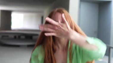 Parlak, minimalist bir odada, kızıl saçlı bir kadın yeşil bir tişörtle dans eder, boşluğu dinamik hareketlerle doldurur, mutluluk ve pozitiflik yayar, neşe ve özgürlük hissi yayar.