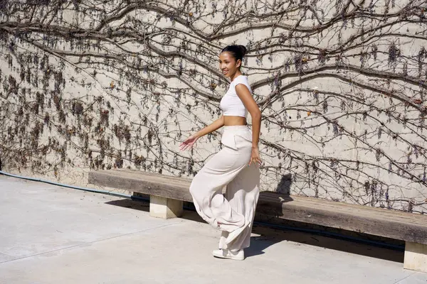 Tarz sahibi bir kadın canlı yeşil sarmaşıklarla bezenmiş taşralı bir duvarın yanında duruyor, modern zarafet ve yaratıcılığın eşsiz bir karışımını sergileyerek, onu gören herkesi büyülüyor.