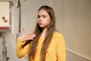 Genç bir kadın canlı sarı bir süveter giyerek dokulu bir duvara karşı düşünceli bir şekilde poz verirken görülebilir. Bu da onun eşsiz yaratıcılığını ve canlı bir şehir ortamında derin iç gözlem yeteneğini gösterir.