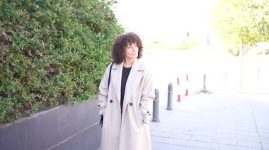 Şık bir kadın şık trençkotunu sergiliyor canlı ve gür yeşilliklerin arasında dolaşırken, sakin ve sakin bir çevrede modern şehir hayatının özünü somutlaştırıyor.
