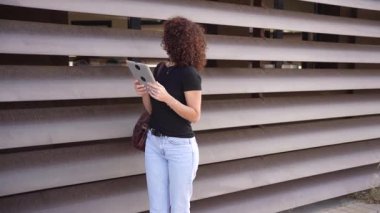 Genç bir kadın tesadüfen kırsal ahşap bir duvara yaslanıyor, tabletine derinden odaklanıyor, modern teknolojiyi hem yaratıcılığı hem de ilhamı teşvik eden rahat bir atmosferle ustaca harmanlıyor.