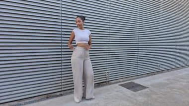 Canlı bir şehir ortamında, modaya uygun genç bir kadın kendine has tarzını sergiliyor, modaya uygun kesilmiş bir üst giysisi ve şık görünüşünü ve tavrını tamamlayan geniş bir pantolon giyiyor.