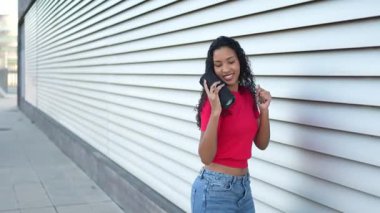 Parlak kırmızı tişörtlü canlı genç bir kadın en sevdiği müzikle dışarıda neşeyle dans ediyor. Portatif bir hoparlörle, günışığıyla dolu modern bir şehir zeminine karşı mutluluk saçıyor.