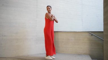 Canlı kırmızı bir elbise giymiş şık bir kadın zarif, minimalist mimari bir zemine karşı duruyor. Olağanüstü zarafetini, özgüvenini ve çağdaş moda anlayışını sergiliyor.