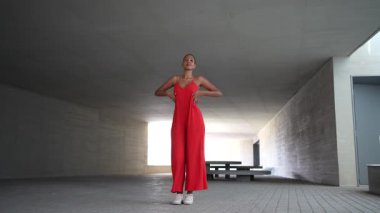 Geniş ve minimalist mimari bir ortamda, yetenekli bir dansçı zarif performansıyla seyirciyi cezbeder, çarpıcı, canlı kırmızı bir elbise giyerken akışkan hareketler sergiler.