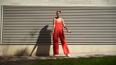 Parlak kırmızı elbiseli büyüleyici bir model, dokulu bir duvara karşı, güzelliğini, karizmasını, zarafetini ve bireyselliğini sergileyerek, varlığını unutulmaz kılıyor.