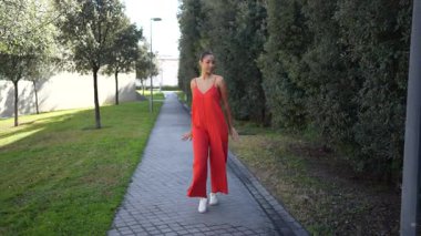 Genç bir kadın canlı kırmızı bir elbiseyle poz veriyor. Etrafı yemyeşil, neşe saçan ve sıcacık gülüşü sahneyi aydınlatıyor.