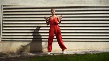 Kırmızı elbiseli kendine güvenen bir kadın çizgili bir duvara karşı poz veriyor. Şık modayla modern bir yaşam tarzını harmanlıyor. Zarafetini ve gençlik ruhunu bu canlı kompozisyonda sergiliyor.