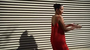 Canlı bir şehir ortamında, şık bir kadın eşsiz bir duvara karşı çarpıcı kırmızı bir elbiseyle poz verir, modern moda anlayışını ve hareketli kişiliğini sergiler, yanından geçen herkesi büyüler.
