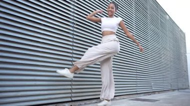 Canlı bir şehir ortamında, modaya uygun giyinmiş şık bir genç kadın ve peruk pantolon neşe içinde dans ediyor, sanatsal dokulu bir arka plana karşı canlı kişiliğini sergiliyor.