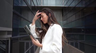 Modern bir şehir ortamında, kendine güvenen bir iş kadını, iş dünyasındaki liderliğini ve yenilikçi ruhunu gözler önüne seren bir tablet bulundurur.