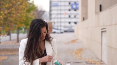 Şık beyaz ceketli şık bir kadın şık bir şehir caddesinde zarif bir şekilde yürüyor, şık bir alışveriş çantası taşıyor ve güzel sonbahar yapraklarına hayran, kendine güveni ve zarafeti yayıyor.