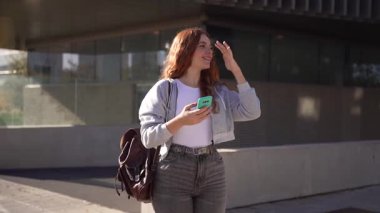 Modern giyinmiş şık bir genç kadın, hareketli bir şehirde dolaşırken akıllı telefonuyla meşgul oluyor, modern moda trendlerinin ve kentsel canlılığın özünü mükemmel bir şekilde yakalıyor.