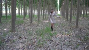 Genç bir çocuk mutlu bir şekilde, uzun ağaçlar, canlı yeşillikler ve düşkün yapraklardan oluşan bir halı ile dolu bir ormanda yürüyor. Doğanın çarpıcı güzelliğini gözler önüne seriyor.