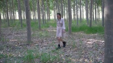 Huzurlu ve huzurlu bir ortamda, genç bir kadın sakin bir ormanın uzun ağaçları arasında zarif bir şekilde duruyor, doğanın güzelliğini ve çevresindeki sakin ortamı somutlaştırıyor.