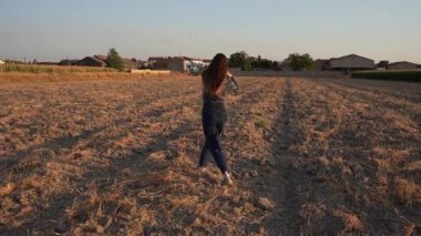 Gündelik giyinmiş bir kadın huzurlu bir sonbahar manzarasında neşeli bir şekilde yürür, doğanın güzelliğini ve sükunetini kucaklayarak huzurlu kırsal alanda her anın tadını çıkarır.