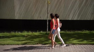 Hayat dolu ve enerji dolu iki genç kadın güneşli bir şehir kaldırımında tesadüfen yürüyorlar, canlı ve canlı bir atmosferi ön plana çıkaran sıcak ve neşeli bir ortam yaratıyorlar.