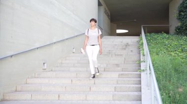 Şık ve modaya uygun bir birey, zarif bir şekilde tasarlanmış bir merdiven üzerinde duruyor. Temiz ve çarpıcı bir mimarinin arka planına karşı zahmetsizce modern tarzı sergiliyor.