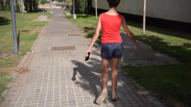 Güneşli bir günde, neşeli genç bir kadın şık bir atlet ve şortla pitoresk bir parkta geziniyor, canlı yaz atmosferini kucaklıyor ve güzel manzaranın tadını çıkarıyor.