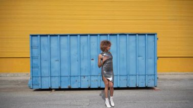 Şık bir model, canlı şehir modasında öne çıkan çağdaş sokak modasının çeşitli bir koleksiyonunu sergileyen parlak sarı ve elektrik mavisi renkli şehir zeminine karşı poz veriyor.