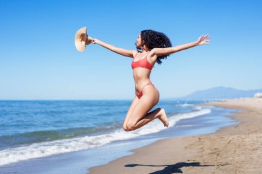 Büyüleyici bir sahnede, bir kadın neşeyle güneşli bir plajda zıplıyor, neşeli ve kaygısız bir yaz havasını mükemmel bir şekilde yansıtırken, kıyı yaşamının inanılmaz güzelliğini vurguluyor.