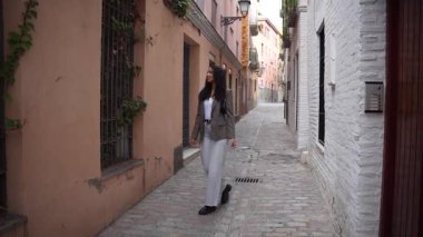 Zarif bir kadın zarif bir şekilde renkli binalar ve ikonik kaldırım taşlarından oluşan bir sokakta yürüyor. Çevresini keşfederken çarpıcı modern şehir tarzını sergiliyor.