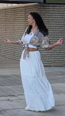 Neşeli bir kadın dışarıda şık bir yaz elbisesi içinde dans eder, modern mimarinin pitoresk bir ortamı ile canlı enerjisini arttırır ve canlandırıcı görsel bir deneyim yaratır.