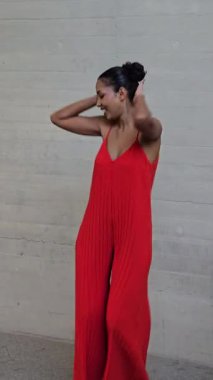 Stüdyoda, kendine güvenen kırmızı elbiseli bir kadın gri bir arka plana karşı poz veriyor, modern moda eğilimlerini ve günümüzün sanatını yansıtan zarafet ve entelektüellik.