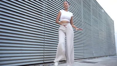 Karakter ve derinlikle dolu kentsel bir ortamda, şık bir kadın kendine güvenerek ileri doğru adım atar, şık bir hasat bluzu giyer, wideleg pantolonla eşleşir, modern ve zarif bir modaya bürünür.